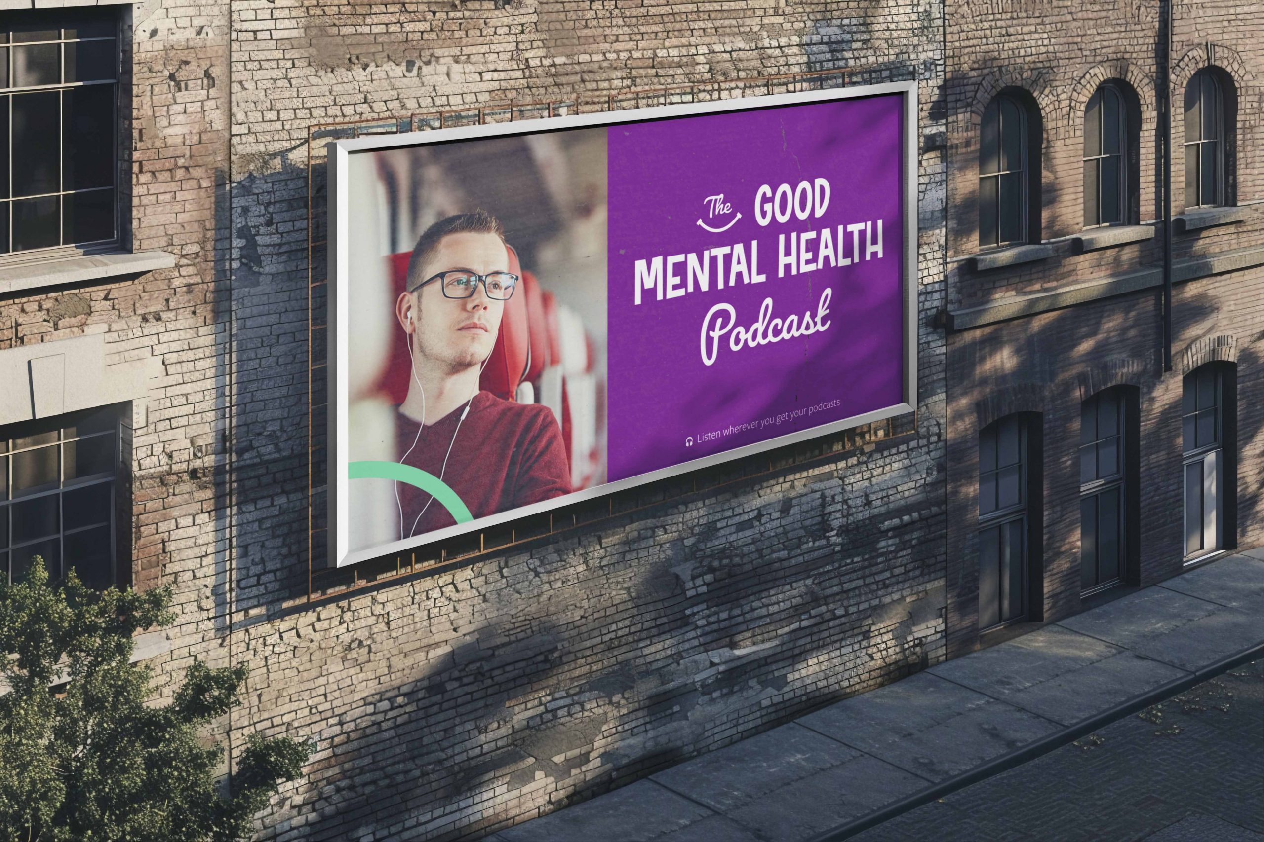 Concept: a billboard on a brick building showing a man in glasses listening on earphones on a train, beside a purple panel with the Good smile mark