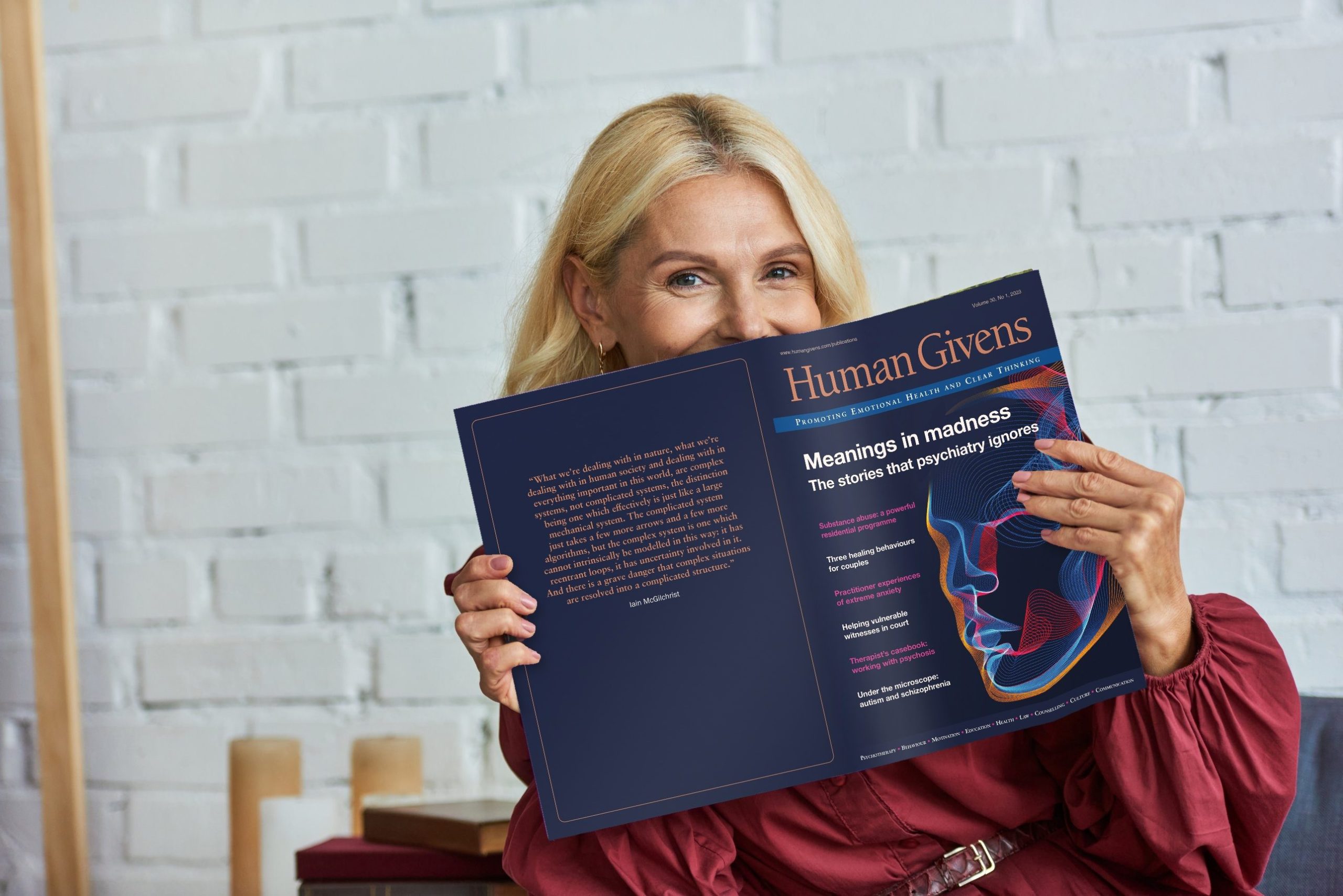 A reader smiling over an open copy of the Human Givens Journal, Volume 30, No. 1, 2023, showing the cover and the inside quote